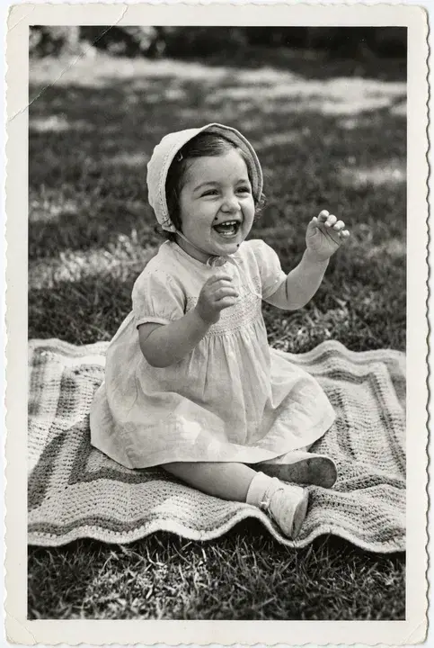 A toddler sitting on a blanket on a lawn, laughing