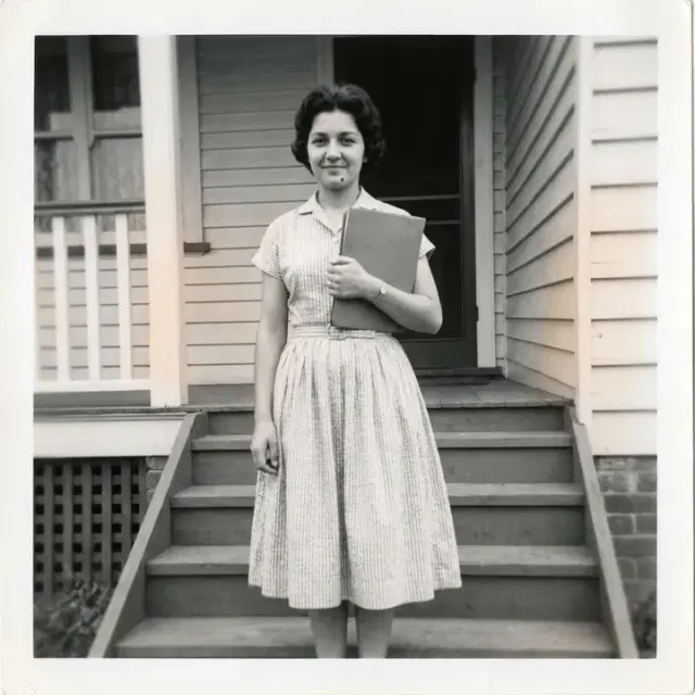 A teenager standing on the front steps of a house holding a folder