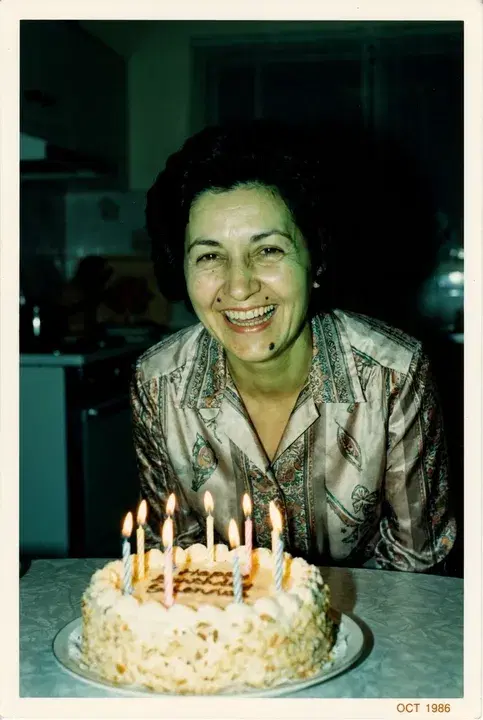 A woman laughing behind a birthday cake with lit candles