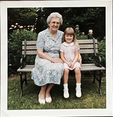 Colour print of a grandmother and a small girl on a park bench.